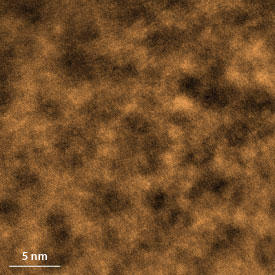 金属ガラスの走査型透過電子顕微鏡（STEM）像。室温まで冷却された後も原子が動くことのできるクラスター領域（顕微鏡写真中の暗い部分）があるのが分かる。